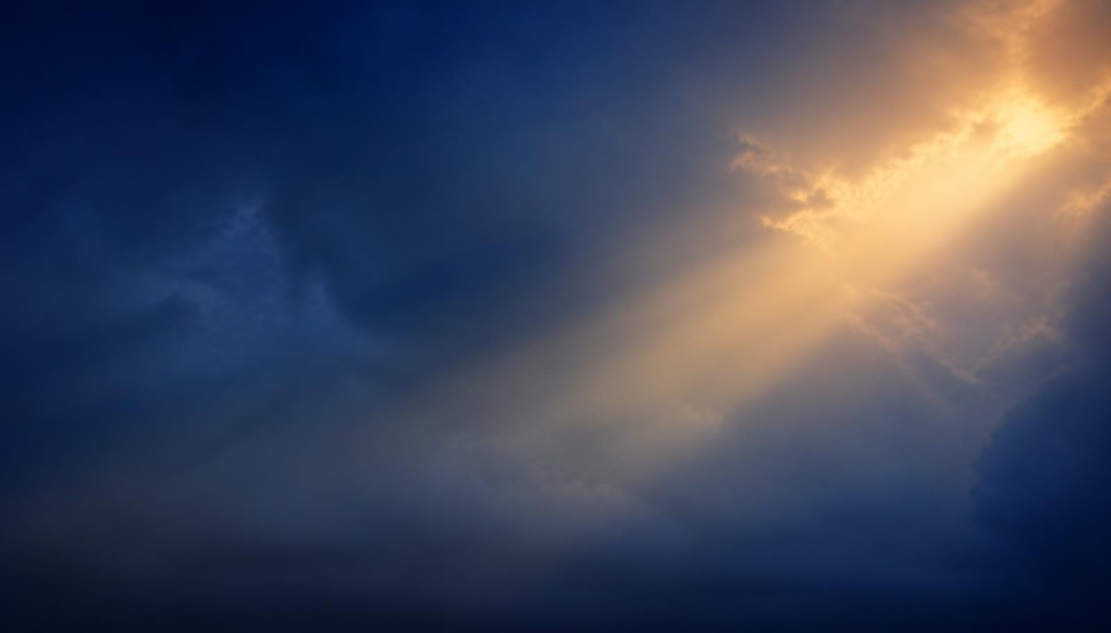 Céu azul profundo com um feixe de luz dourada atravessando as nuvens